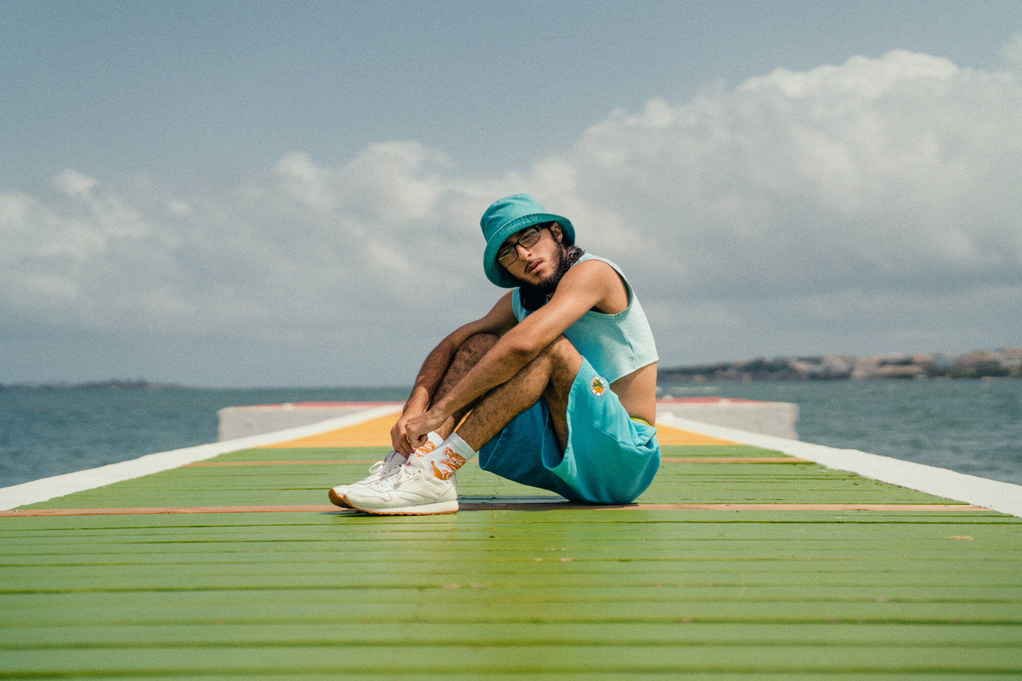 Color photograph of a person seated on a long green bridge.